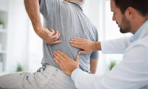 Doctor examining a patient's back, feeling for issues with the vertebras dorsales.