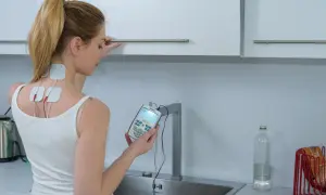 Mujer con electrodos en el cuello y la espalda, sosteniendo un dispositivo para aprender como usar electroestimulador.