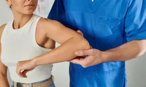 Fisioterapeuta examina el brazo derecho de una mujer, buscando la causa de su dolor.