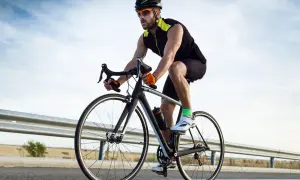 Ciclista con espondilolistesis pedalea en su bicicleta por una carretera rural, disfrutando del aire libre y el ejercicio.