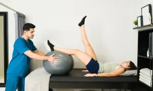 Fisioterapeuta ayuda a paciente con hiperlordosis lumbar ejercicios usando balón.