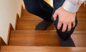 Persona con dolor rodilla al subir escaleras, sujetando su pierna con la mano.