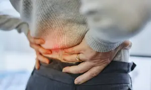 Persona con dolor de espalda baja y orina frecuente, sujetando su cintura.
