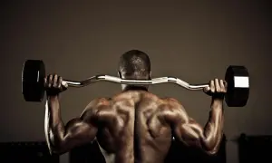 Hombre musculoso en el gym realizando ejercicios para la parte baja de la espalda con barra.
