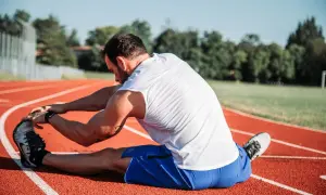 Atleta estirando en pista, cuidando sus isquiotibiales para evitar una rotura.
