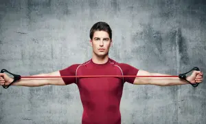 Hombre realizando ejercicios con gomas para brazos y hombros, estirando la banda roja con ambas manos.