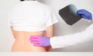 Médico examina radiografía mientras palpa la espalda de un paciente, buscando la causa del dolor en las costillas flotantes.