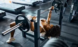 Mujer concentrada realizando press banca con barra en un gimnasio.