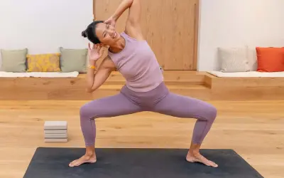 Mujer sonriente practica yoga, un deporte que fortalece cuerpo y mente, en una sala luminosa.