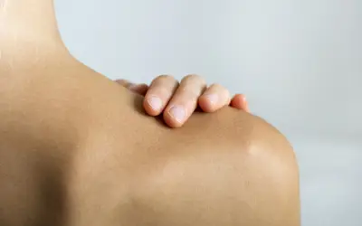Mano tocando el hombro, resaltando la articulación acromioclavicular.