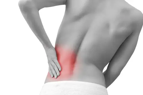 Persona con dolor lumbar izquierdo, con la mano apoyada en la zona afectada, resaltada en rojo.