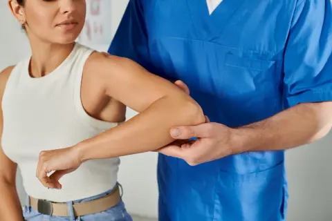 Fisioterapeuta examina el brazo derecho de una mujer, buscando la causa de su dolor.