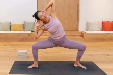 Mujer sonriente practica yoga, un deporte que fortalece cuerpo y mente, en una sala luminosa.