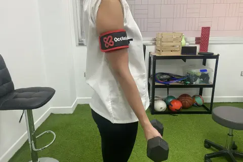 Persona con banda de oclusión en el brazo realiza ejercicios con mancuerna, parte de la rehabilitacion fractura humero ejercicios.