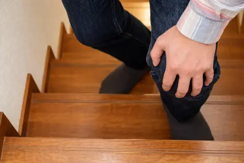 Persona con dolor rodilla al subir escaleras, sujetando su pierna con la mano.