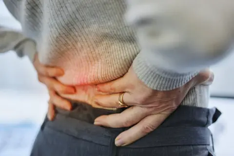 Persona con dolor de espalda baja y orina frecuente, sujetando su cintura.