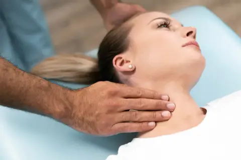 Manos de terapeuta ajustando el cuello rectificado de una mujer en una camilla.