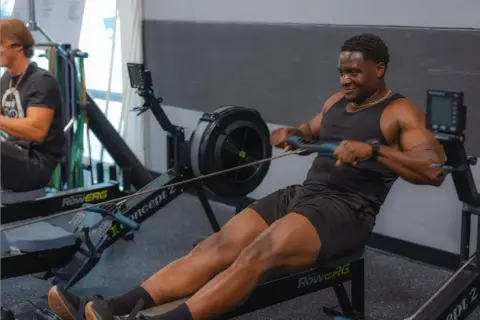 Hombre sonriendo mientras hace remo, un excelente ejercicio de cardio.