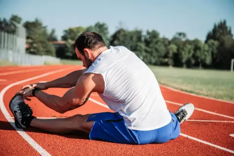 Atleta estirando en pista, cuidando sus isquiotibiales para evitar una rotura.