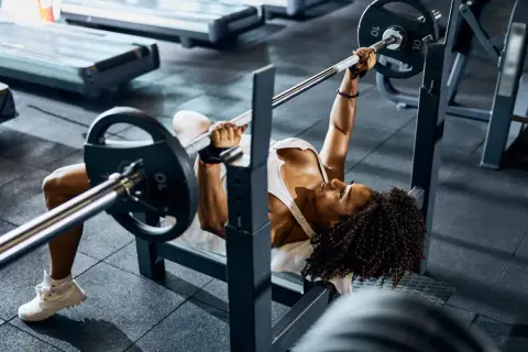 Mujer concentrada realizando press banca con barra en un gimnasio.