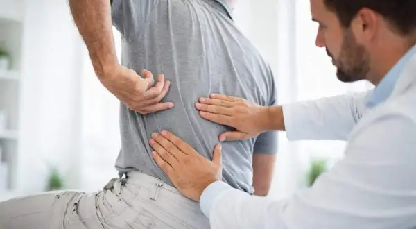 Doctor examining a patient's back, feeling for issues with the vertebras dorsales.