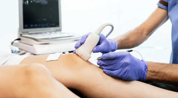 Profesional aplica tratamiento con corriente galvanica en rodilla, guiado por ecografía.