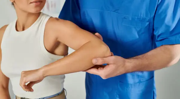 Fisioterapeuta examina el brazo derecho de una mujer, buscando la causa de su dolor.