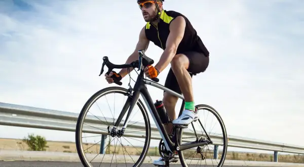 Ciclista con espondilolistesis pedalea en su bicicleta por una carretera rural, disfrutando del aire libre y el ejercicio.