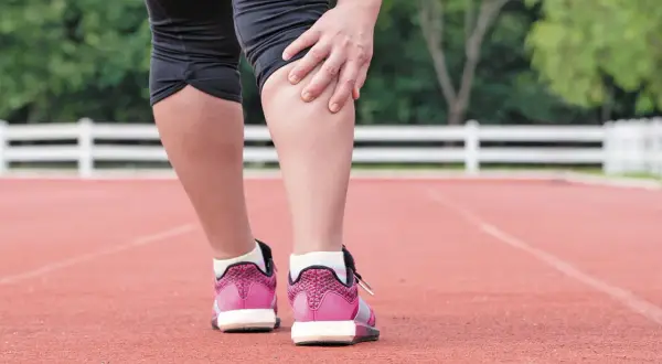 Corredora se toca la pierna, sintiendo dolor en el gemelo musculo tras el esfuerzo.