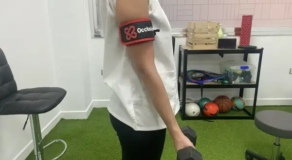 Persona con banda de oclusión en el brazo realiza ejercicios con mancuerna, parte de la rehabilitacion fractura humero ejercicios.