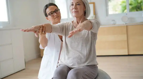 Fisioterapeuta ayuda a una mujer mayor a mejorar su equilibrio y fuerza, trabajando en diferentes niveles de Berg.
