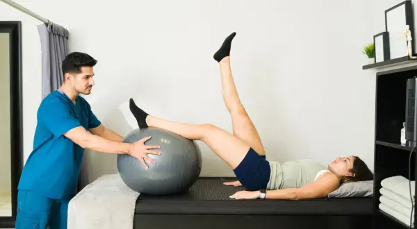 Fisioterapeuta ayuda a paciente con hiperlordosis lumbar ejercicios usando balón.