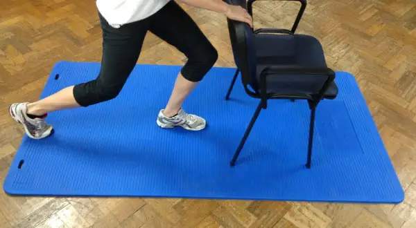 Persona realiza zancada asistida por silla, un ejercicio clave para la artrosis de cadera.
