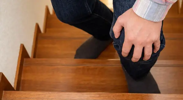 Persona con dolor rodilla al subir escaleras, sujetando su pierna con la mano.