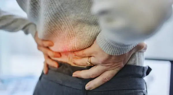Persona con dolor de espalda baja y orina frecuente, sujetando su cintura.
