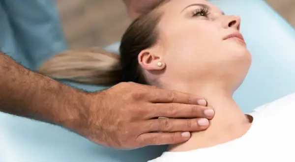 Manos de terapeuta ajustando el cuello rectificado de una mujer en una camilla.