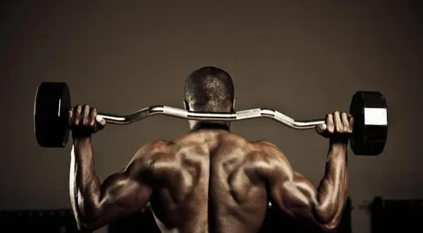 Hombre musculoso en el gym realizando ejercicios para la parte baja de la espalda con barra.
