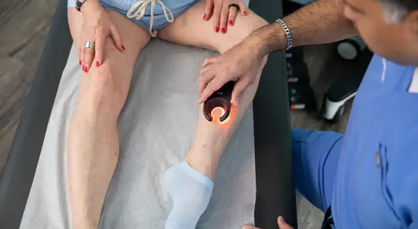 Médico examina pierna izquierda con dispositivo de luz para diagnosticar dolor.