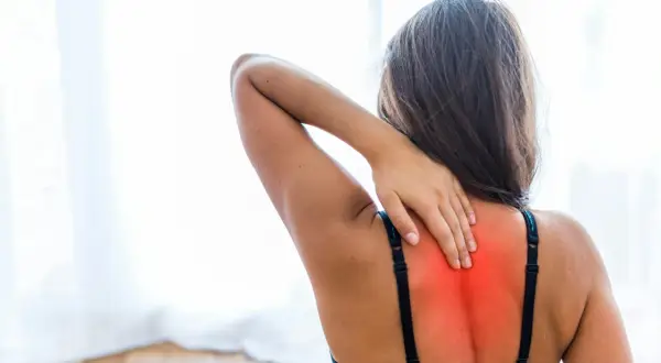 Mujer con mano en la espalda alta, sintiendo dolor. Busca cómo quitar una contractura en la espalda alta.