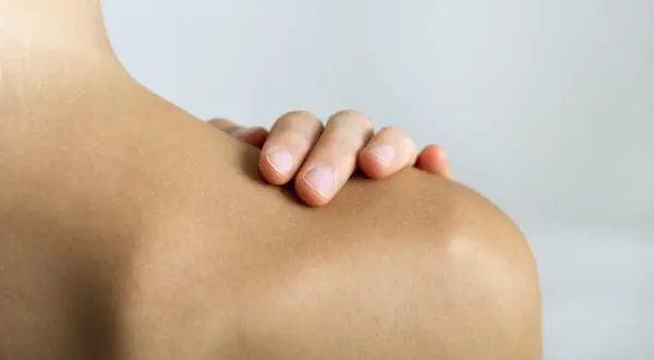 Mano tocando el hombro, resaltando la articulación acromioclavicular.