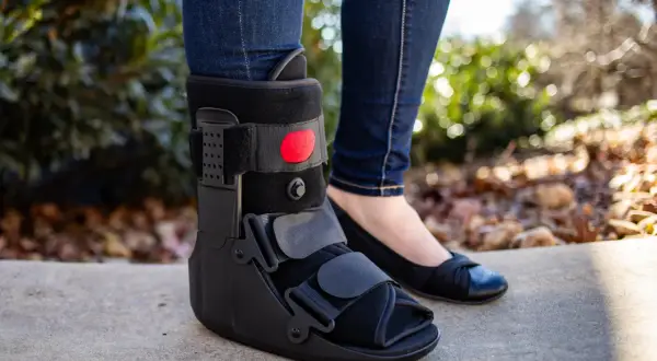 Piernas con jeans y una bota walker negra. Se puede quitar la bota walker para dormir, permitiendo usar un zapato cómodo.