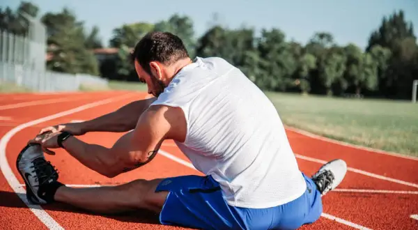 Atleta estirando en pista, cuidando sus isquiotibiales para evitar una rotura.