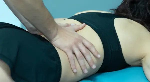 Manos de fisioterapeuta trabajando en la zona lumbar de una mujer, aliviando el crujido espalda.