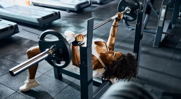 Mujer concentrada realizando press banca con barra en un gimnasio.