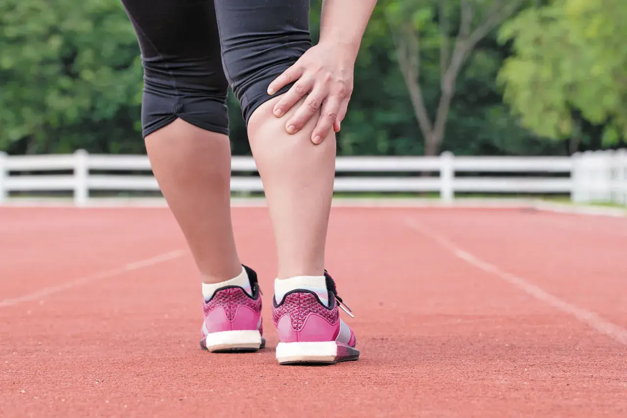 Corredora se toca la pierna, sintiendo dolor en el gemelo musculo tras el esfuerzo.