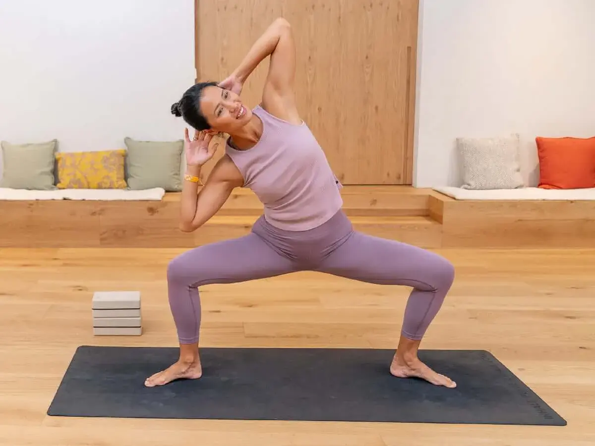 Mujer sonriente practica yoga, un deporte que fortalece cuerpo y mente, en una sala luminosa.