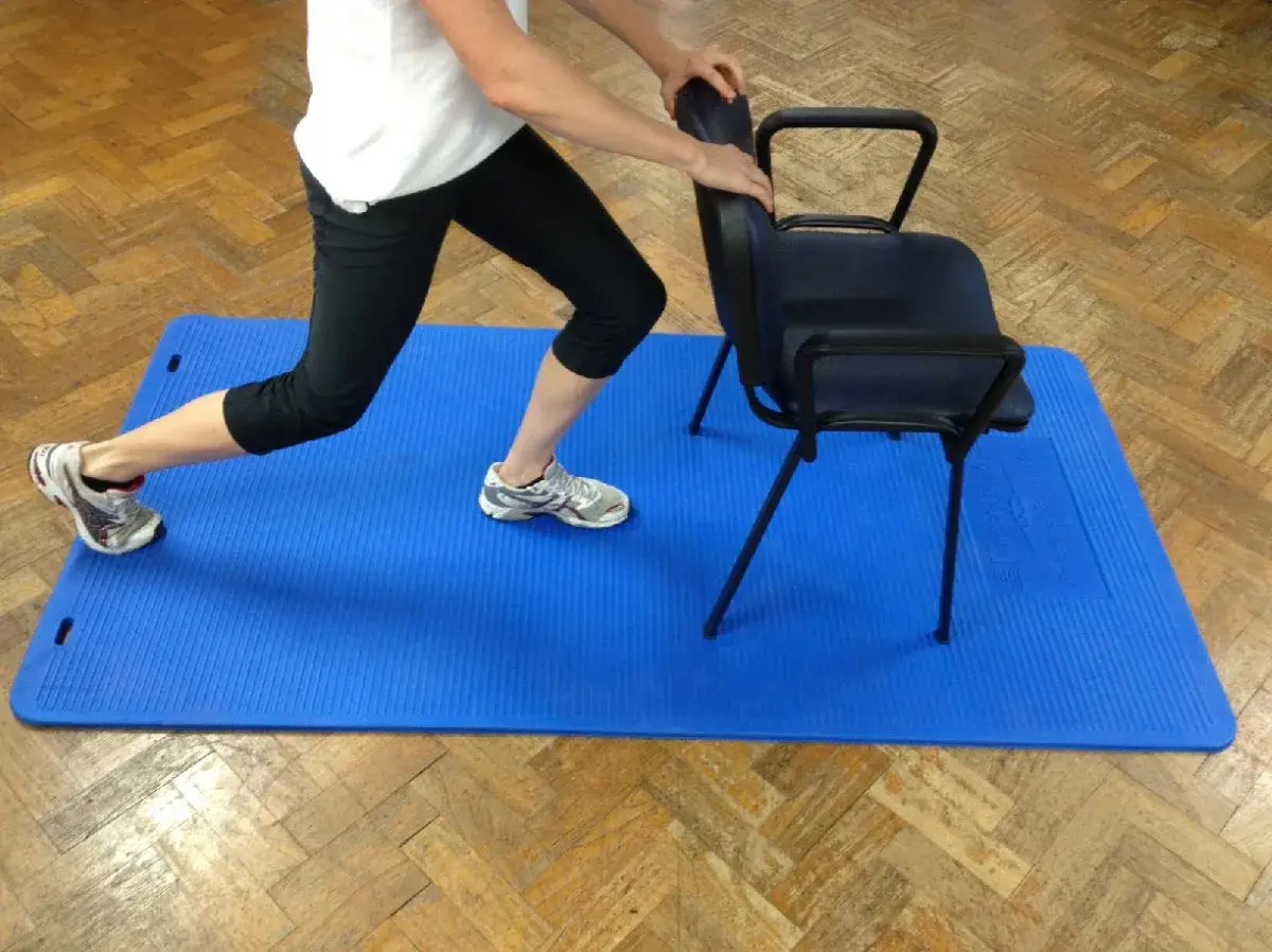 Persona realiza zancada asistida por silla, un ejercicio clave para la artrosis de cadera.
