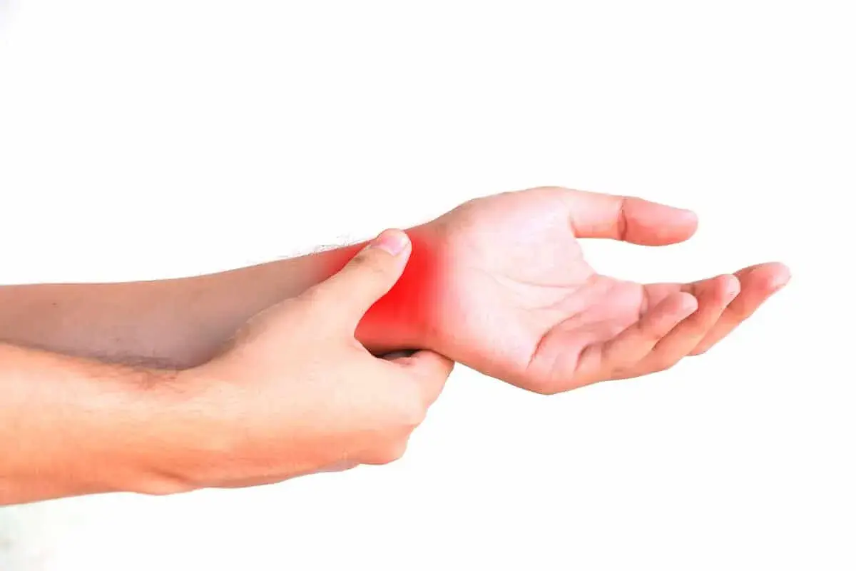Una mano se presiona la muñeca, con una zona roja indicando dolor. ¿Cómo saber si tengo la muñeca abierta?