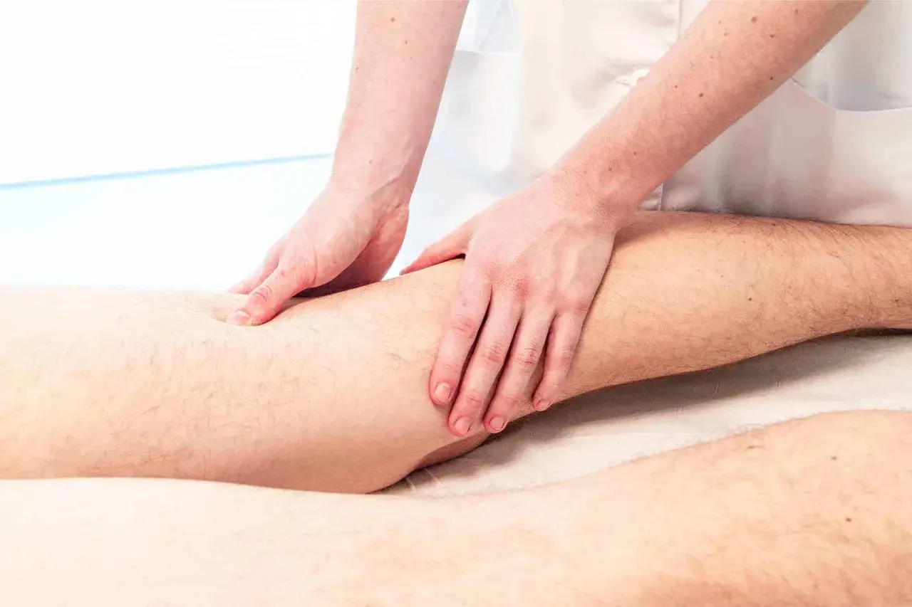 Manos expertas aplican masoterapia en fisioterapia para aliviar tensión muscular en la pierna.