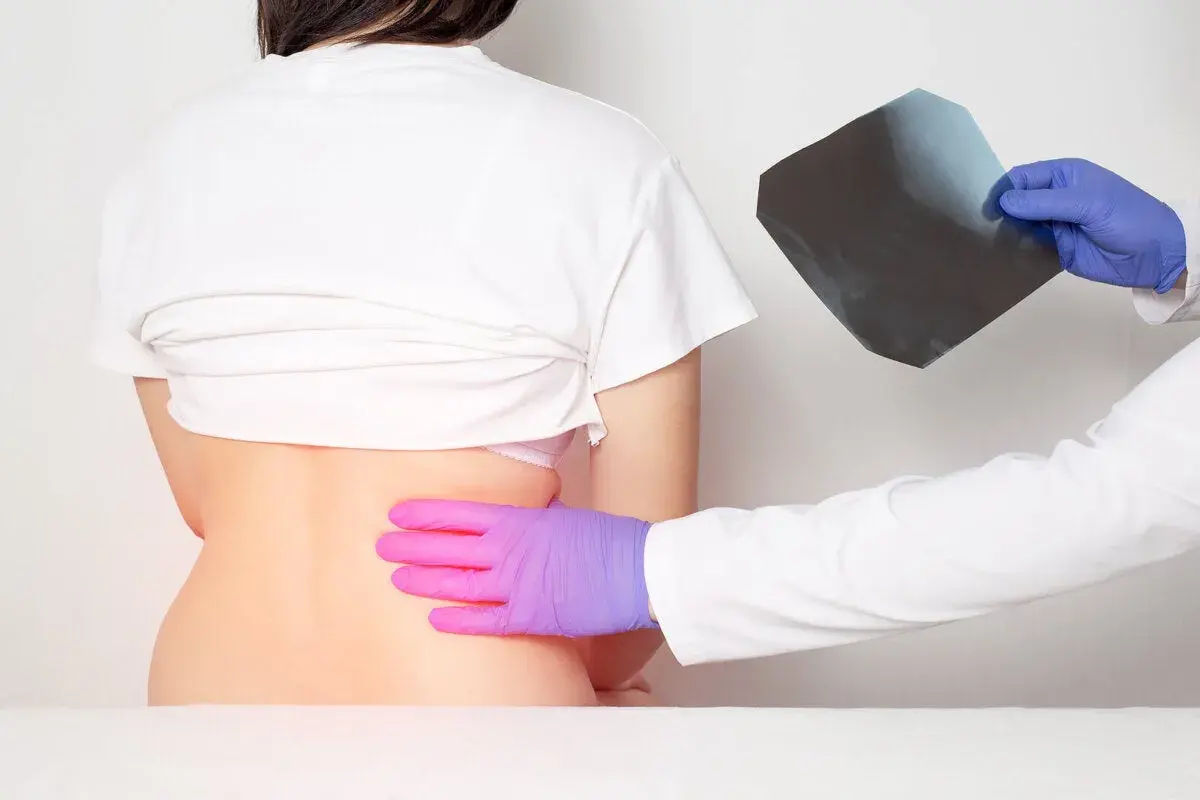 Médico examina radiografía mientras palpa la espalda de un paciente, buscando la causa del dolor en las costillas flotantes.